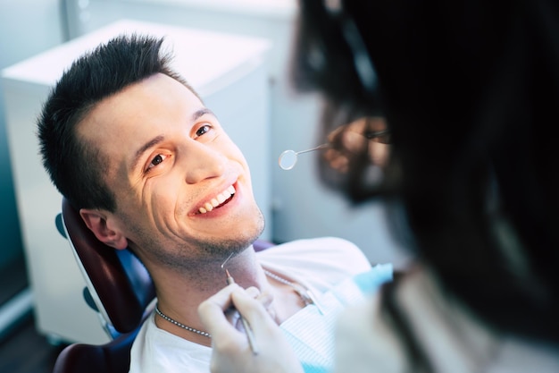 A man in a dental chair with a special napkin over his neck is having an examination of his tooth condition from a dentist in a professional clinic