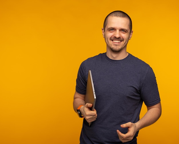 Man developer or freelancer holding laptop and weared in grey tshirt at orange background