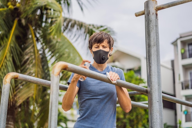 Man disinfects horizontal bar before sports A man in a medical mask plays sports during the coronavirus epidemic