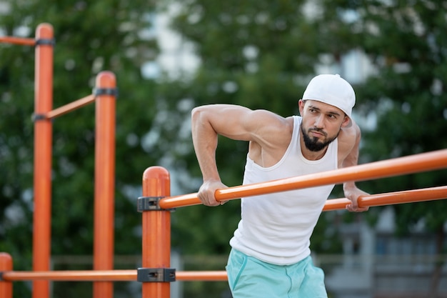 A man does push-UPS on the bars on the street at the day