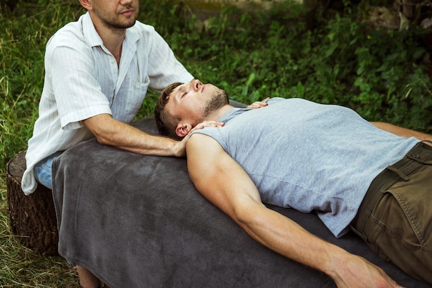 Man doing osteopathic head massage to a guy in nature 2