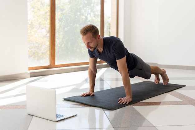 Man doing yoga pose looking at laptop