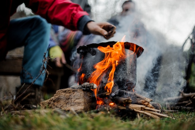 Man drawn by hand to the black pan with a dish standing on the bonfire over the group of friends