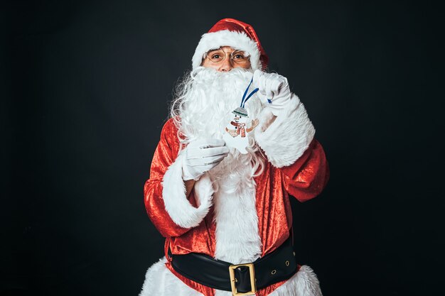 Man dressed as Santa Claus holding the figure of a snowman, on black background. Concept of Christmas, Santa Claus, gifts, celebration.