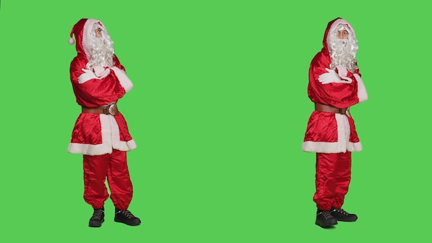 Man dressed as santa feeling impatient, waiting for something while he stands over full body greenscreen backdrop. Saint nick character pacing around the studio, christmas eve holiday.