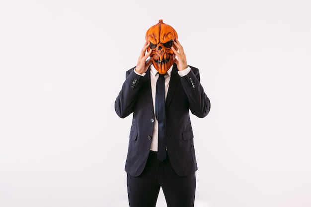 Man dressed in jacket suit, blue tie and Jack-o-lantern pumpkin mask, hands on head, like crazy. Halloween and carnival celebration concept.