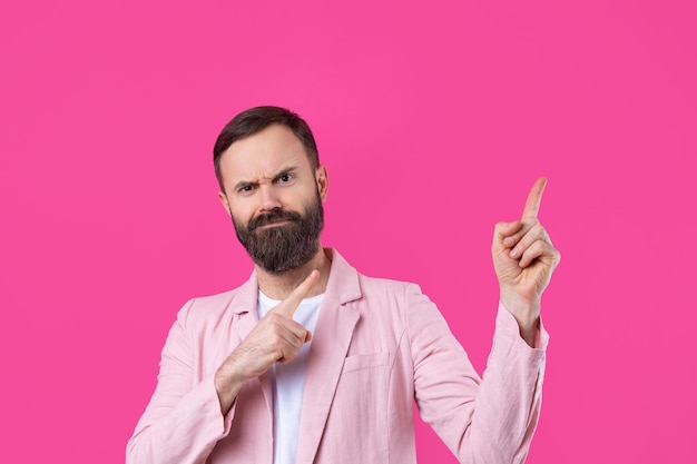 A man dressed in a pink jacket indicates the direction on a pink isolated background