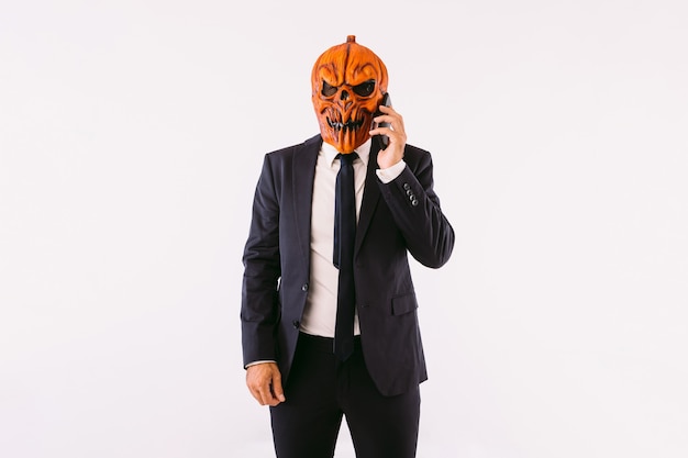 Man dressed in a suit jacket, blue tie and Jack-o-lantern pumpkin mask, talking on the mobile phone, like crazy. Halloween and carnival celebration concept.