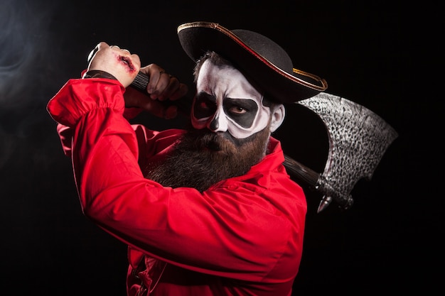 Man dressed up like a pirate for halloween holding and axe over black 