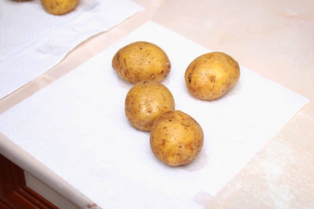 A man dries raw washed potatoes with paper towels and napkins to bake them in foil in the oven