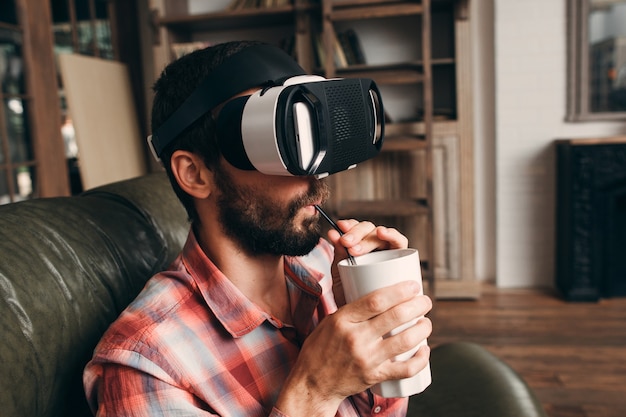 Man drinking cocktail while using vr glasses at home.