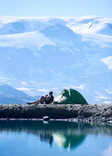 Man drinking tea near tent in mountains