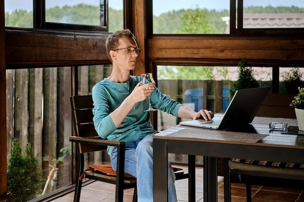 Man drinking wine and chatting in messenger on laptop