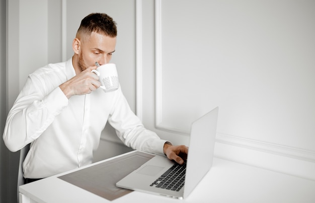 A man drinks coffee working at a laptop in his kitchen