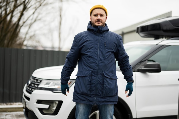 Man driver wear jacket and yellow hat against his american SUV car with roof rack in cold weather