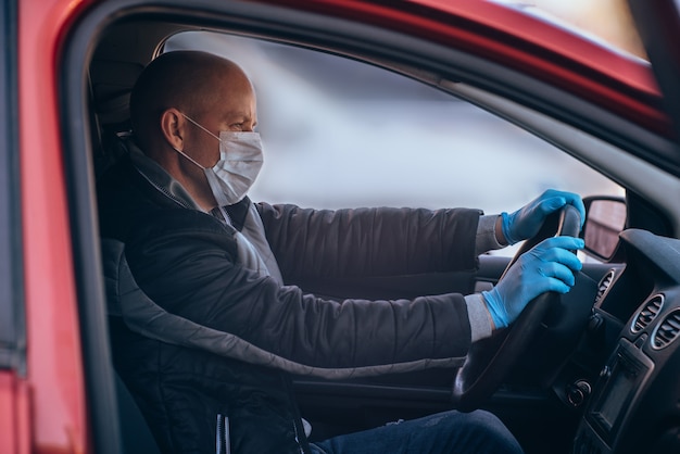 A man driving a car in a protective medical mask and gloves. Safe drive in a taxi during a pandemic coronavirus.