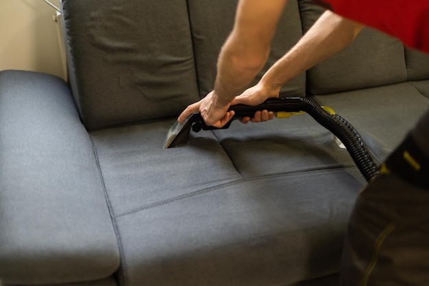 Man dry cleaner's employee cleaning sofa with professionally extraction method