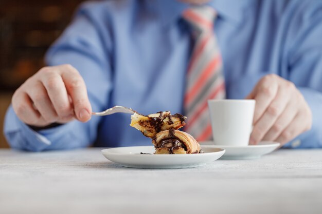 Man eating strawberry cheesecake in cafe drinking coffee