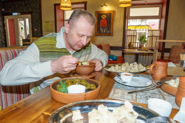 A man eats food in a restaurant with a picture of a woman on the wall behind him.