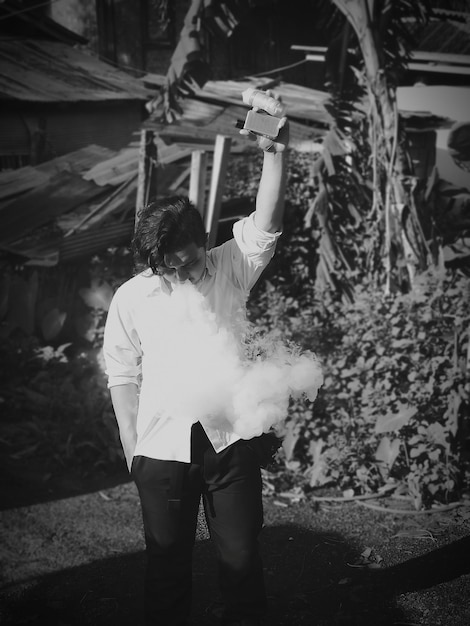 Photo man emitting smoke while holding equipment against plants