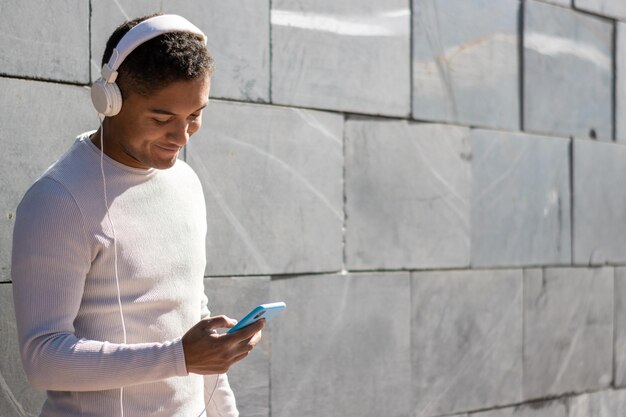 Photo man enjoying listening to music through headphones with his phone, horizontal view with sunlight