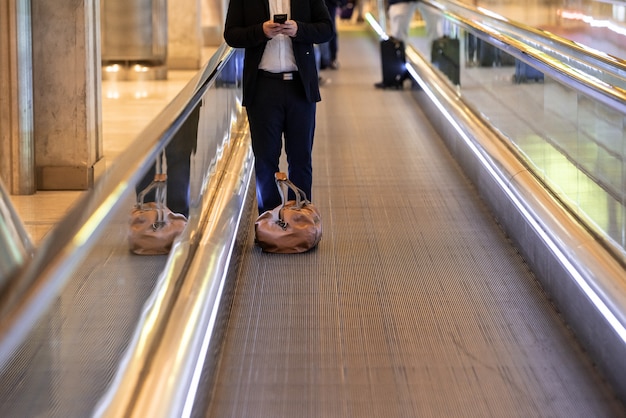 Man on escalator at the airport using mobile phone with luggage