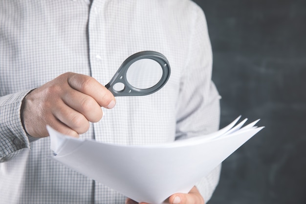 Man examines documents with a magnifying glass .