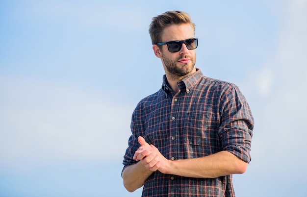 Man eyewear model outdoors blue sky background. Handsome guy wear sunglasses. Perfect vision. Eyes health. Fashionable sunglasses. Hipster man in trendy sunglasses. Ultraviolet protection concept.