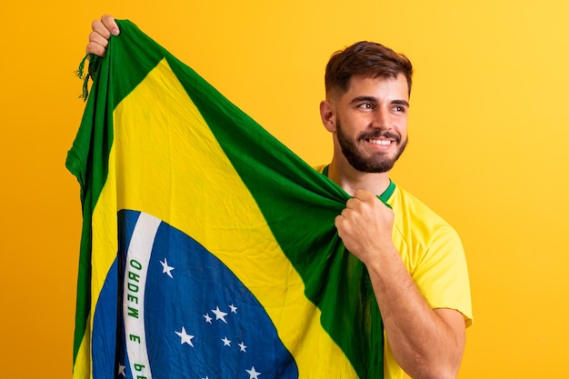 Man fan holding a Brazilian flag yellow background. Brazil colors in background, green, blue and yellow. Elections, soccer or politics.