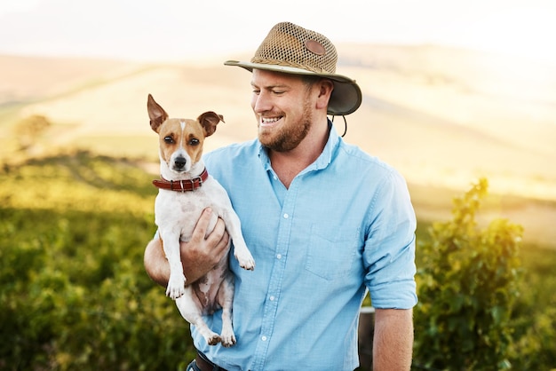 Photo man farmer and dog with smile in vineyard with hat connection or care with growth plants and fruits person animal and happy for grapes production and countryside for sustainability in italy