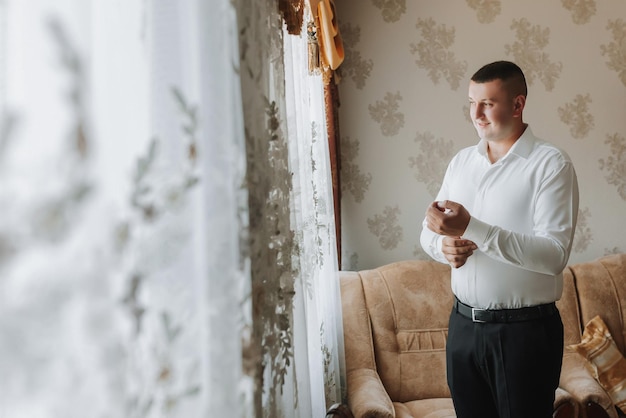 the man fastens the buttons on his shirt sleeve The groom is preparing for the wedding