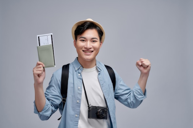 Man feeling happy about summer trip holding passport with plane tickets and backpack raising hands up in celebration gesture