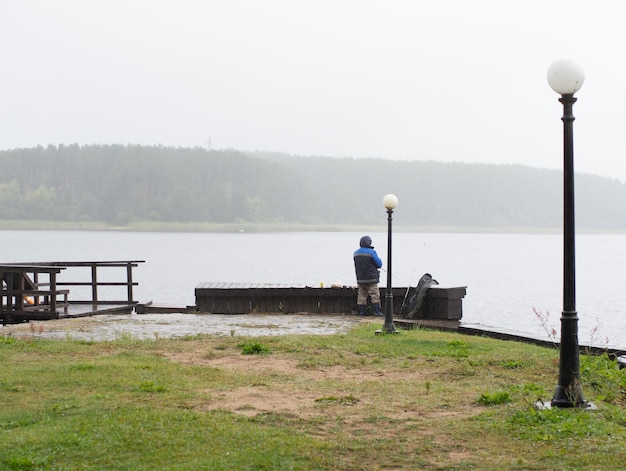 Man fishing on the pier on a rainy and foggy day