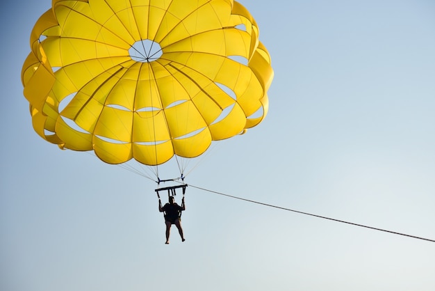 A man flies a parachute over the sea at sunset