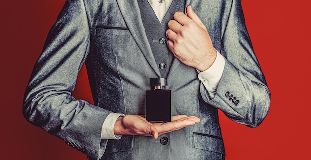 Man in formal suit bottle of perfume closeup Men perfume in the hand on suit background Fragrance smell