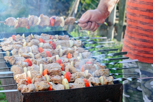 A man fries meat with vegetables on iron skewers on the grill Cooking shashlik