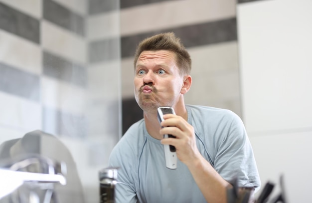 Man in front of a mirror shaves off his stubble with machine