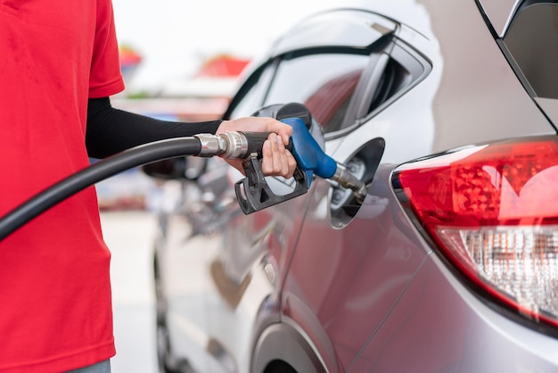 Man gas station attendant in red uniform holding fuel pump nozzle refueling in car at gas station