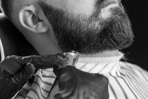 Man getting his beard trimmed with electric razor in barbershop Black and white image