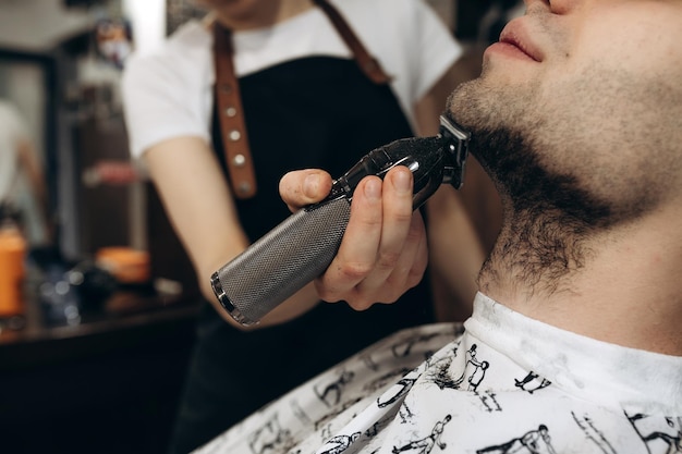 Man getting his beard trimmed with electric razor shaving beard in a barbershop