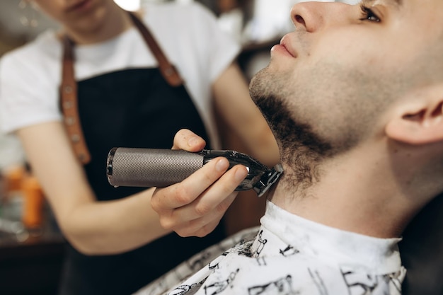 Man getting his beard trimmed with electric razor shaving beard in a barbershop