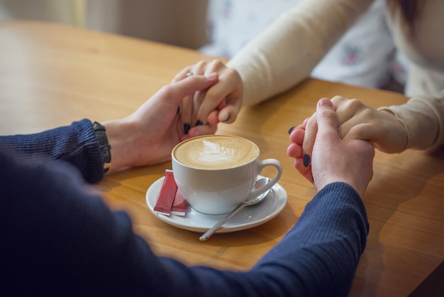 A man and a girl hold hands at the table, a cup of coffee