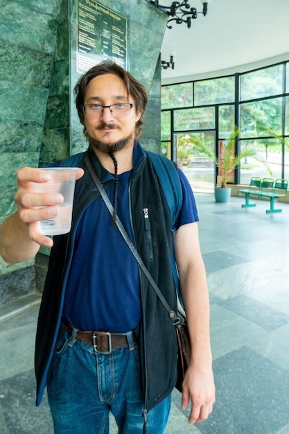 A man gives mineral thermal water in the disposable cup at the pumproom closeup