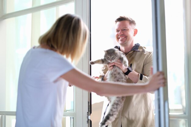 Man giving grey cat to woman through door. Overexposure of pets concept