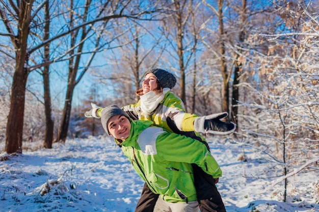 Man giving his girlfriend piggyback in winter forest. Couple in love having fun