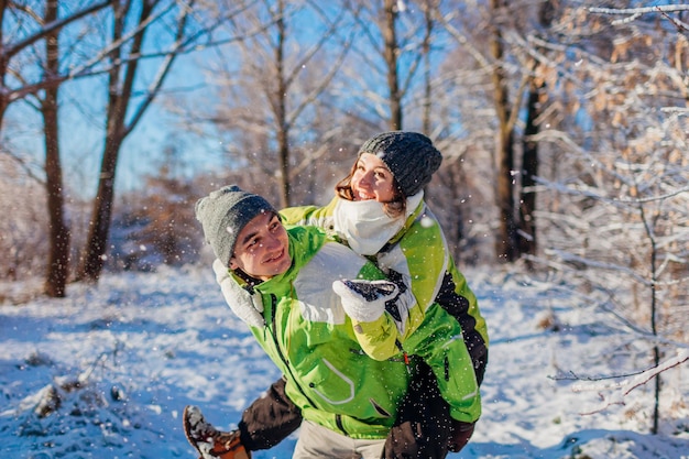 Man giving his girlfriend piggyback in winter forest couple in love having fun