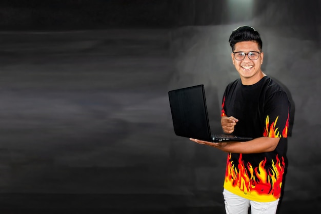 Man in glasses and polo shirt with flames holds a laptop. Technology concept on black background