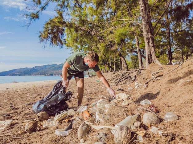 Man in gloves pick up plastic that pollute sea and forest Problem of spilled rubbish trash garbage on the beach sand caused by manmade pollution campaign to clean volunteer in concept