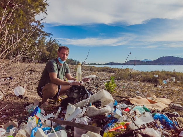 Man in gloves pick up plastic that pollute sea and forest Problem of spilled rubbish trash garbage on the beach sand caused by manmade pollution campaign to clean volunteer in concept