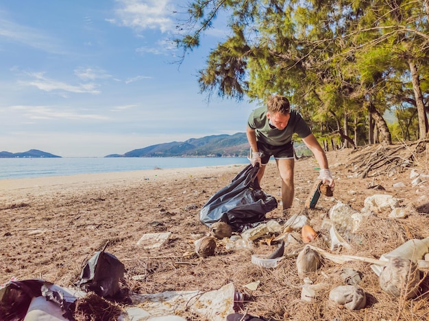 Man in gloves pick up plastic that pollute sea and forest Problem of spilled rubbish trash garbage on the beach sand caused by manmade pollution campaign to clean volunteer in concept